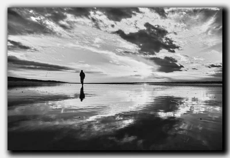 Zwart-wit foto van mensen die wandelen op het Noordzeestrand bij een ondergaande zon